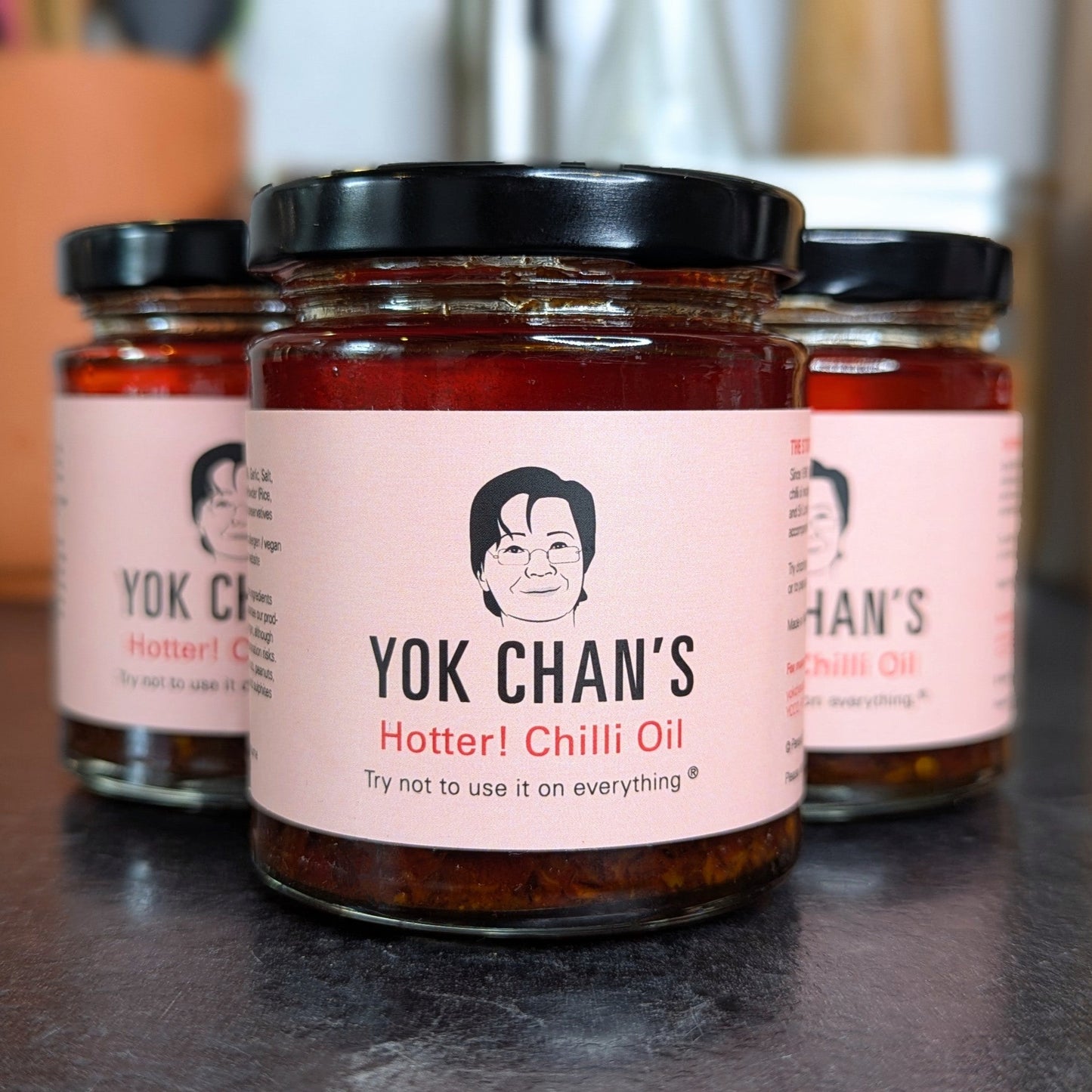 Three jars of Yok Chan's Chilli Oil on a dark surface with a blurred background