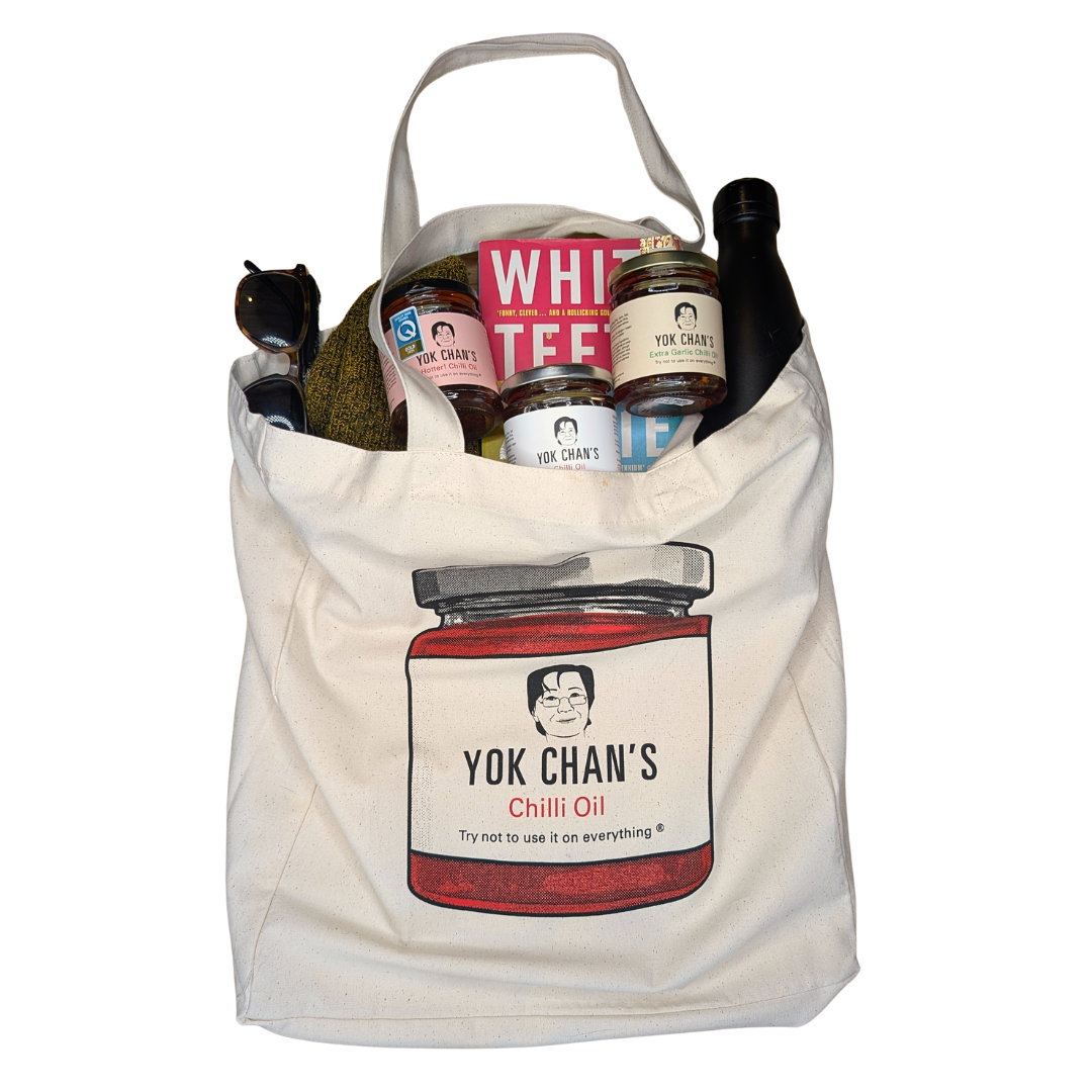 A canvas tote bag featuring a printed illustration of a jar labeled 'Yok Chan's Chilli Oil' with a cartoon face. The bag is filled with various items, including jars, a bottle, and a box, and is photographed against a plain white background.